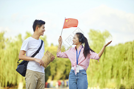 拿着旗帜男孩女导游向游客介绍景点背景