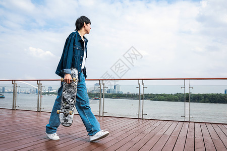 拿着滑板走路的男性高清图片