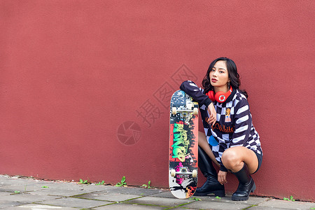 极限运动女拿滑板靠墙的女性形象背景