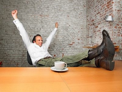 双脚翘在办公桌上的商务人士伸懒腰图片