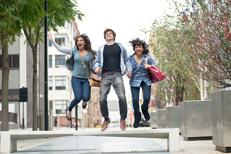 3个年轻人在街上跳跃牵手高清图片素材