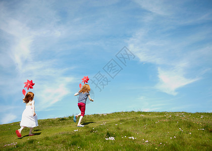 开心小女孩绿色草坪上拿着风车奔跑的两个小女孩背景