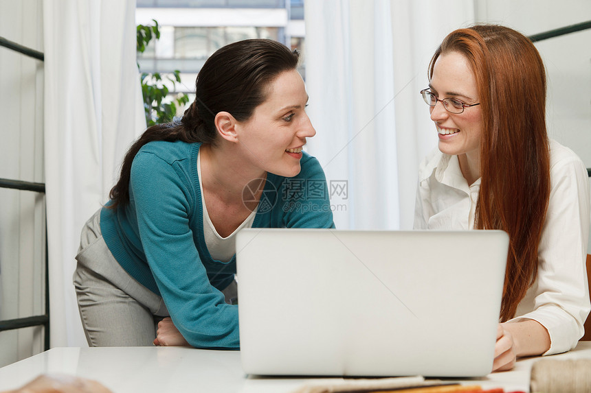 两个女人在笔记本电脑后面相互微笑图片