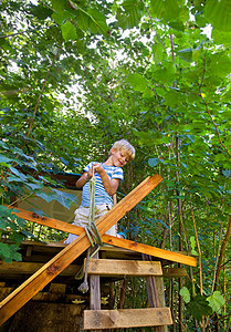站在梯子上的男孩男孩把绳子系在树屋上背景