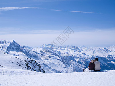 阿尔卑斯山滑雪一对情侣坐在雪地里拥抱背景