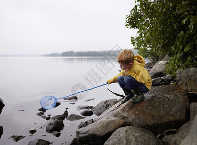 背着渔网的男孩小男孩蹲在岩石上钓鱼背景