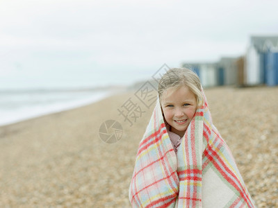 小女孩在海滩上蜷缩在毯子里旅行高清图片素材