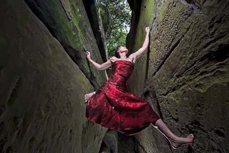 身着红色连衣裙的女子自由攀爬砂岩烟囱岩石缝隙高清图片