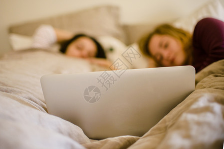 便携性两个年轻的女性朋友躺在床上看笔记本电脑背景