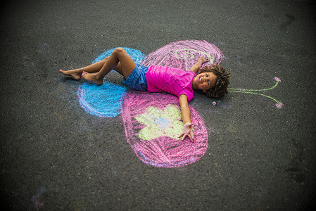 光脚小女孩小女孩躺在粉笔蝴蝶翅膀之间的地板上背景