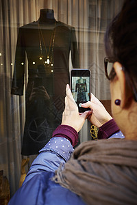中年妇女在商店橱窗里拍照使用手机拍照图片