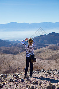 年轻女子站在岩石上，仰望美景图片