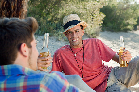 三个人坐在书上坐在沙滩上喝啤酒的年轻朋友背景