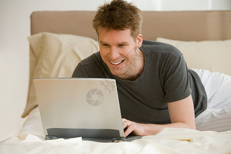 在床上用笔记本电脑的男子在家里高清图片素材