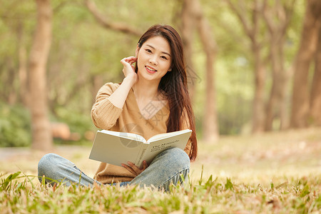 年轻女性坐在草地上看书图片素材
