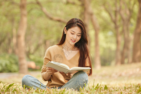 年轻女性坐在草地上看书图片素材