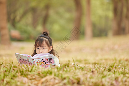 小女孩趴在草地上读童话故事图片素材