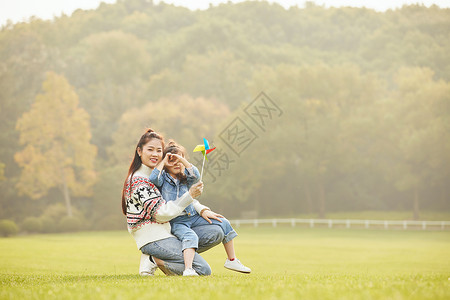 坐在风筝上飞温馨母女坐在草坪玩风车背景