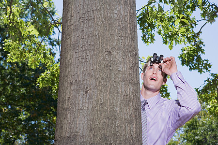 在树后用双筒望远镜的人衬衫高清图片素材