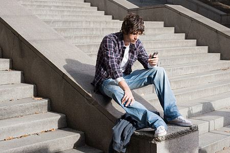 坐在台阶上玩手机的男孩背景图片
