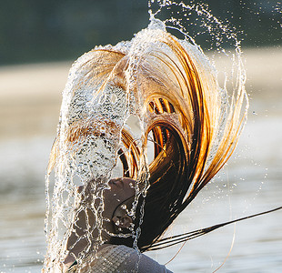 年轻女子在水中甩湿头发的头和肩膀图片