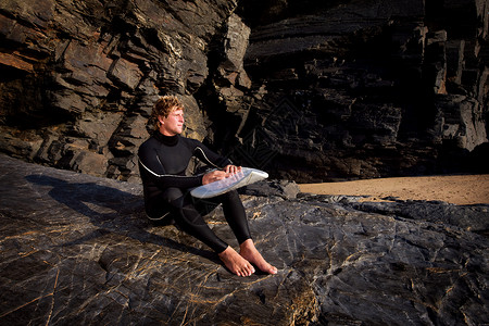 穿着潜水服坐在大石头上休息的男人图片