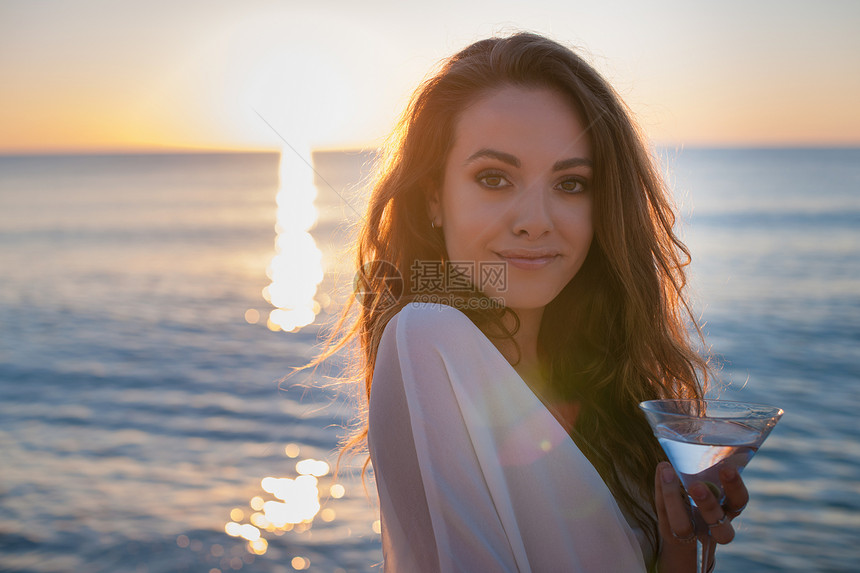 意大利撒丁岛卡斯蒂达斯日落时分带鸡尾酒海滩上的年轻女子的肖像图片