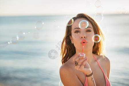 意大利撒丁岛卡斯蒂达斯海滩上吹泡泡的年轻女人的肖像高清图片