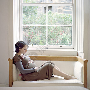 坐在靠窗座位上抱着肚子的中年孕妇画像高清图片