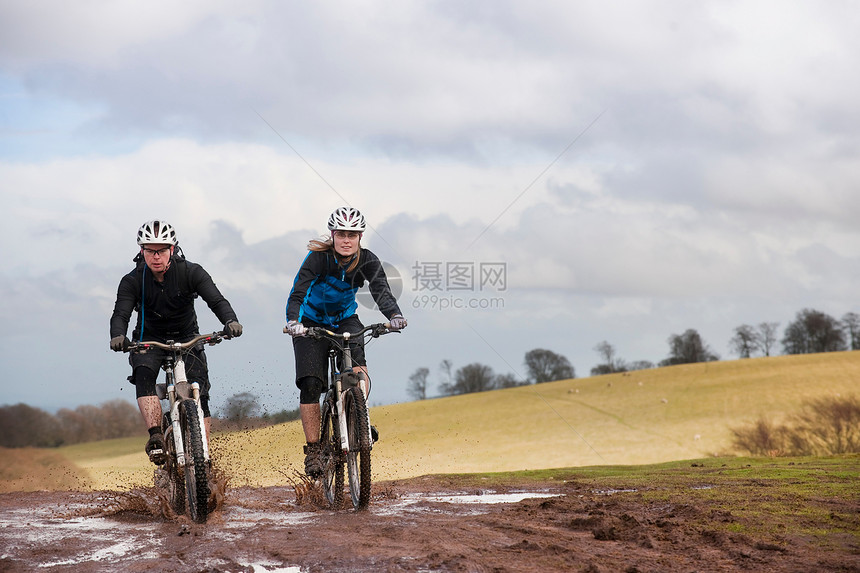 一对夫妇骑自行车穿过泥泞的水坑