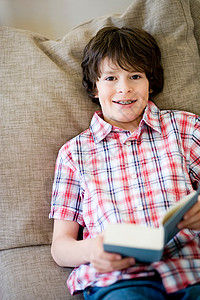 男孩躺在沙发上手里拿着一本书背景图片
