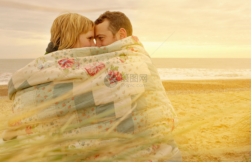 一对夫妇在海滩上的毯子下拥抱图片