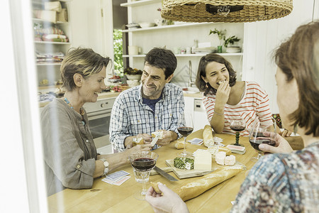 外国人在厨房在餐桌上喝红酒和打牌的成年朋友背景