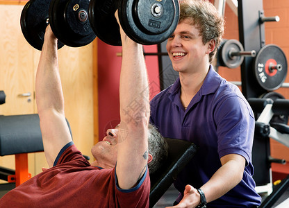 教练在健身房帮助男子举重图片