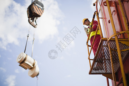 在石油钻机上指挥起重机的工人背景图片