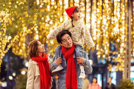 家人冬天夜晚爸爸妈妈抱着女儿一起逛街购物背景