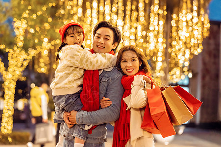 家人冬天夜晚爸爸妈妈抱着女儿一起逛街购物背景
