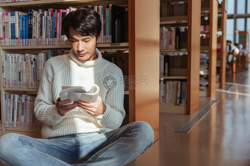 青年男性倚靠在书架上看书图片
