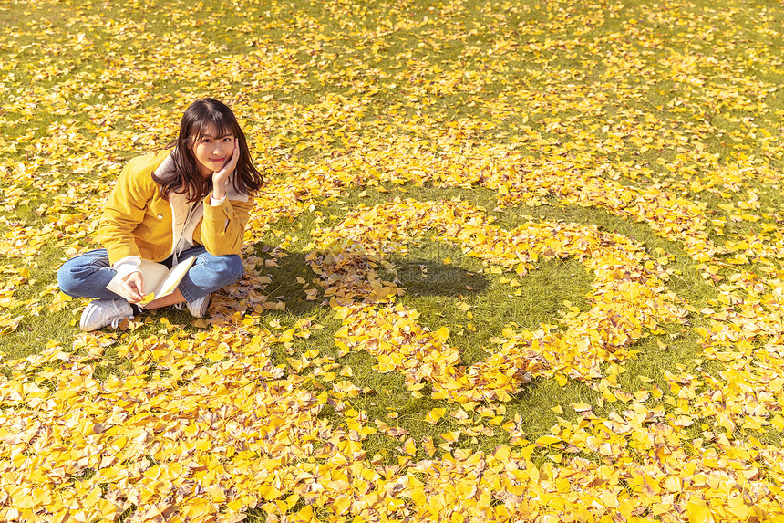 坐在铺满银杏叶的草坪上看书的女孩图片