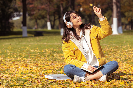 坐在铺满银杏叶的草坪上听音乐的女孩背景