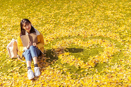 可爱图形坐在铺满银杏叶的草坪上看书的女孩背景