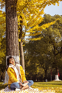 蹲在树下的女孩在银杏树下休息的女大学生背景