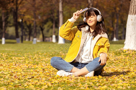 坐在满地银杏叶下听音乐的女孩背景图片