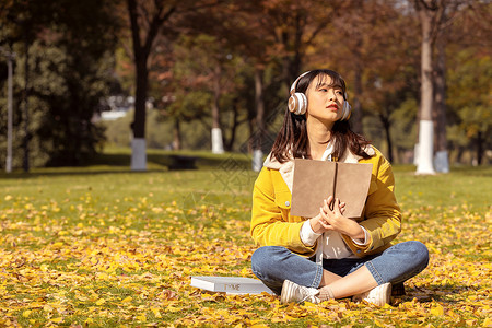 坐在满地银杏叶下听音乐的女孩背景图片