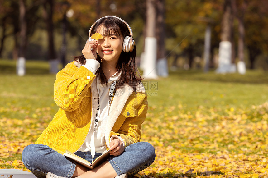 坐在草坪上手举银杏叶的女孩图片