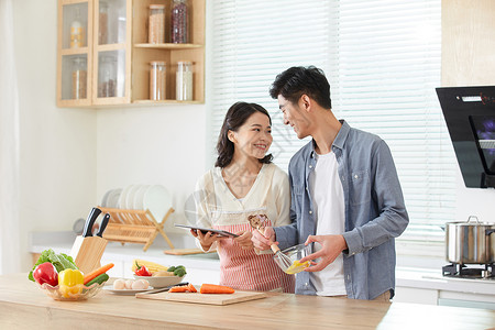 年轻夫妻拿着平板电脑学习做菜背景图片