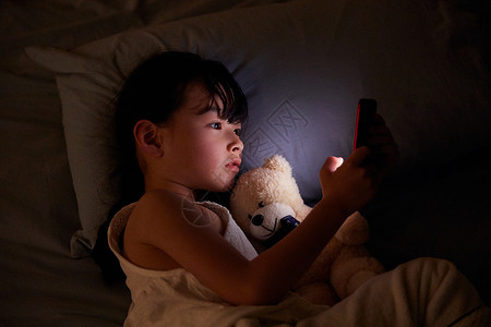 小女孩躺在床上玩手机背景图片