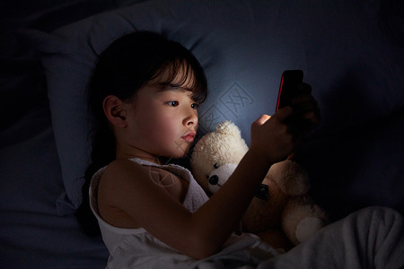 小女孩躺在床上玩手机高清图片