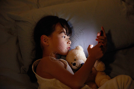 小女孩夜晚躺床上玩手机高清图片
