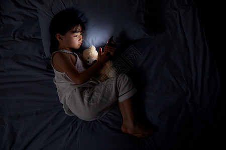 小女孩夜晚躺床上玩手机背景图片